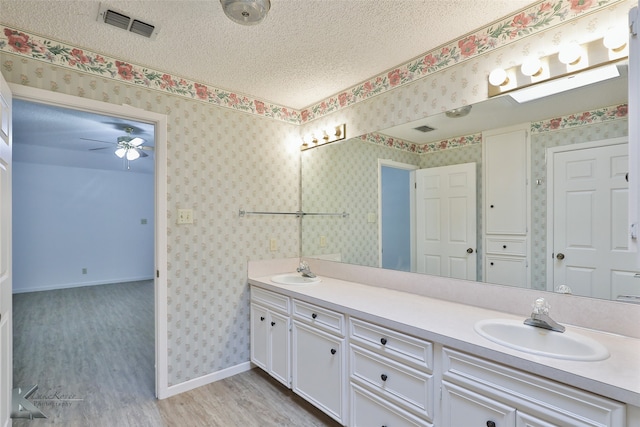 bathroom featuring ceiling fan, wood-type flooring, a textured ceiling, and double vanity