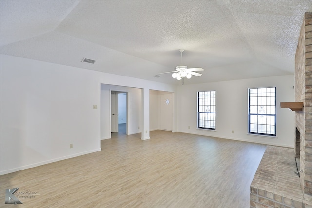 unfurnished living room featuring lofted ceiling, a textured ceiling, light wood-type flooring, ceiling fan, and a fireplace