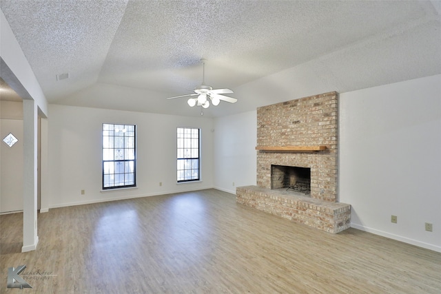 unfurnished living room with lofted ceiling, light hardwood / wood-style floors, a brick fireplace, ceiling fan, and brick wall