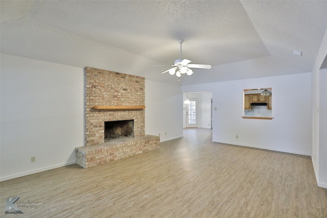 unfurnished living room featuring a brick fireplace, a textured ceiling, light wood-type flooring, and ceiling fan