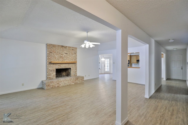 unfurnished living room featuring a textured ceiling, ceiling fan, a fireplace, hardwood / wood-style flooring, and brick wall