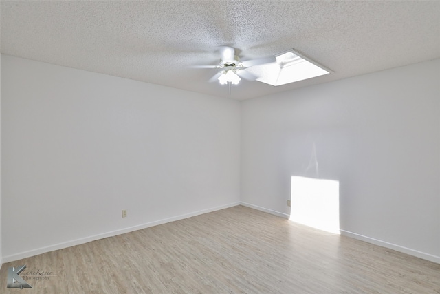 unfurnished room featuring ceiling fan, a skylight, light hardwood / wood-style flooring, and a textured ceiling