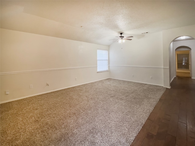 empty room with ceiling fan, a textured ceiling, dark colored carpet, and vaulted ceiling