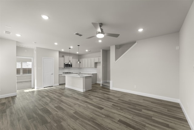 kitchen with pendant lighting, an island with sink, sink, ceiling fan, and dark wood-type flooring