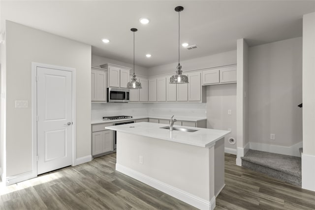 kitchen with appliances with stainless steel finishes, dark hardwood / wood-style floors, pendant lighting, sink, and a center island with sink