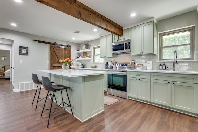 kitchen with appliances with stainless steel finishes, dark wood-type flooring, a barn door, and a center island