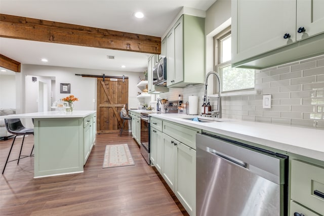 kitchen featuring a kitchen island, a barn door, green cabinets, appliances with stainless steel finishes, and hardwood / wood-style floors