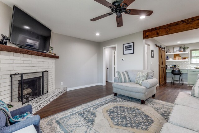 living room with ceiling fan, a fireplace, a barn door, and wood-type flooring