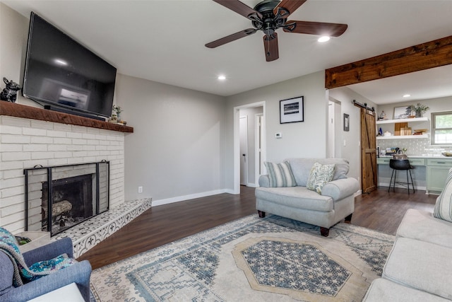 living room featuring dark hardwood / wood-style floors, a fireplace, a barn door, and ceiling fan