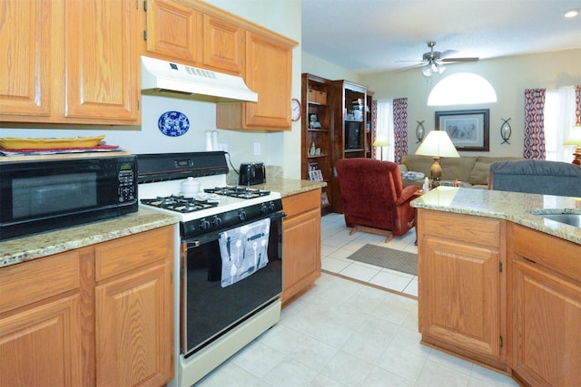 4821 Worthing Dr, Garland, TX 75043 - kitchen featuring under cabinet range hood, range with gas stovetop, black microwave, a ceiling fan, and light stone counters