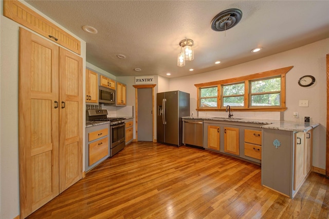 kitchen featuring appliances with stainless steel finishes, sink, light hardwood / wood-style floors, light stone countertops, and a textured ceiling