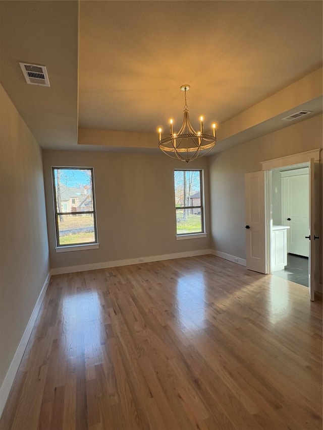 spare room featuring hardwood / wood-style flooring, a raised ceiling, and a chandelier