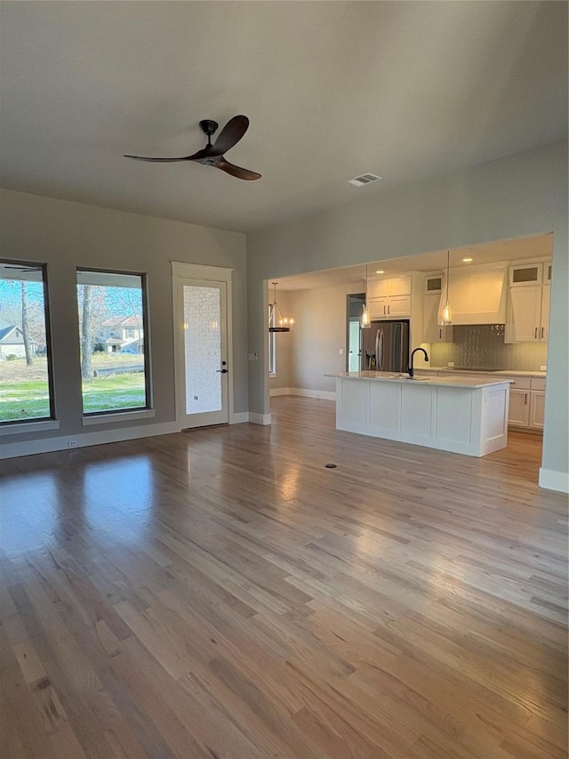 unfurnished living room featuring sink, ceiling fan with notable chandelier, and light wood-type flooring