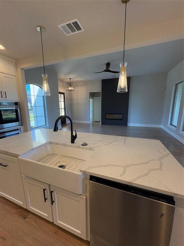 kitchen featuring decorative light fixtures, ceiling fan with notable chandelier, white cabinets, light stone counters, and sink