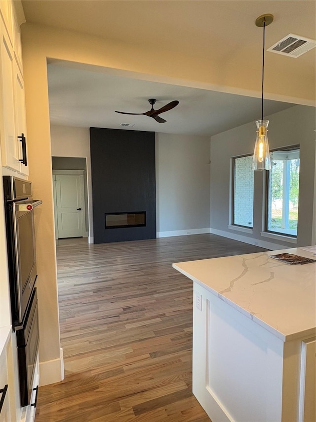 kitchen featuring hardwood / wood-style floors, white cabinets, decorative light fixtures, a large fireplace, and ceiling fan