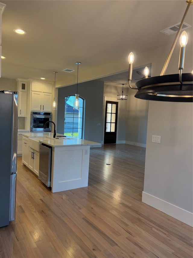 kitchen featuring appliances with stainless steel finishes, decorative light fixtures, white cabinetry, a kitchen island with sink, and hardwood / wood-style flooring