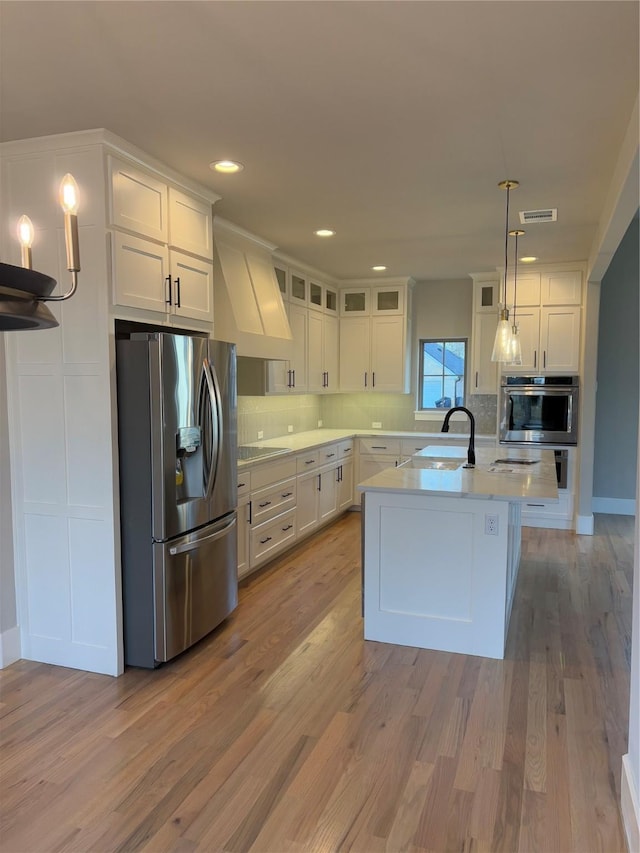 kitchen with a center island with sink, pendant lighting, sink, stainless steel appliances, and white cabinets