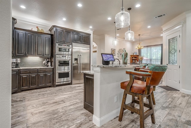 kitchen with a breakfast bar, stainless steel appliances, light hardwood / wood-style flooring, decorative light fixtures, and a center island with sink