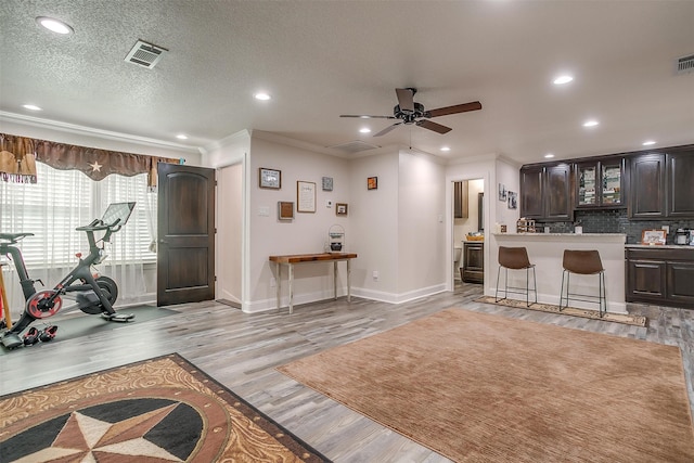 living room featuring ceiling fan, a textured ceiling, light hardwood / wood-style flooring, and ornamental molding