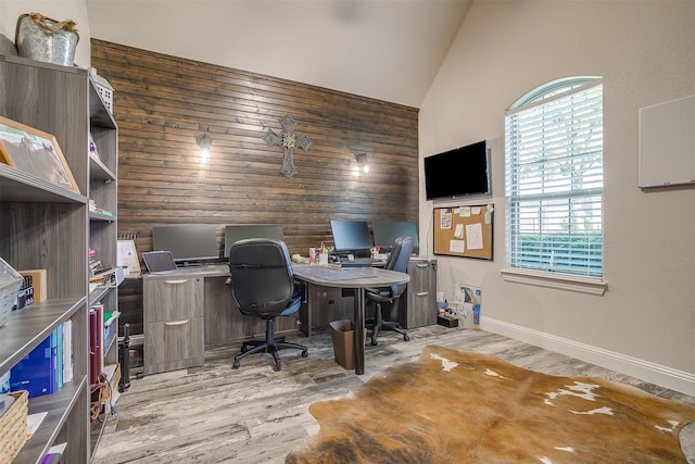 office area with light hardwood / wood-style flooring, wood walls, and high vaulted ceiling