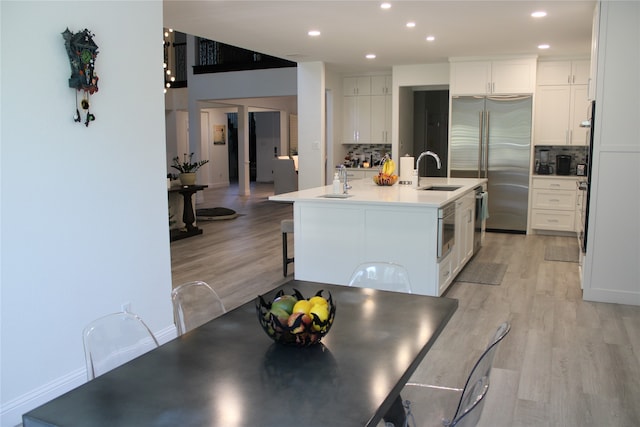 kitchen featuring an island with sink, light hardwood / wood-style floors, white cabinetry, backsplash, and built in refrigerator