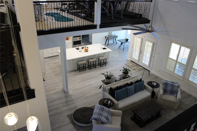 living room featuring a towering ceiling, light hardwood / wood-style flooring, sink, and ceiling fan