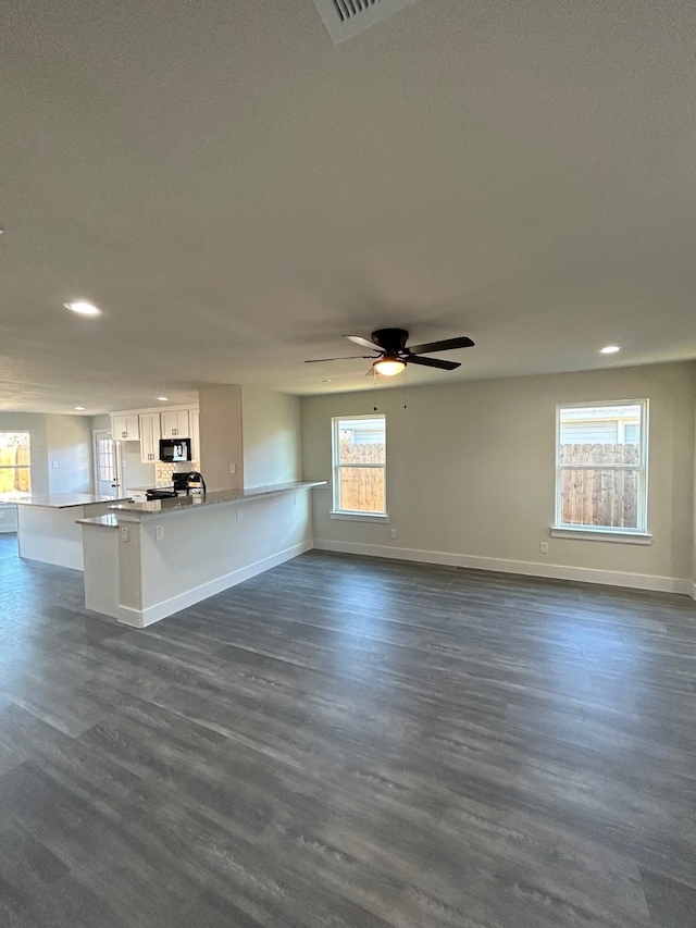 unfurnished living room with dark wood-type flooring, ceiling fan, and a healthy amount of sunlight