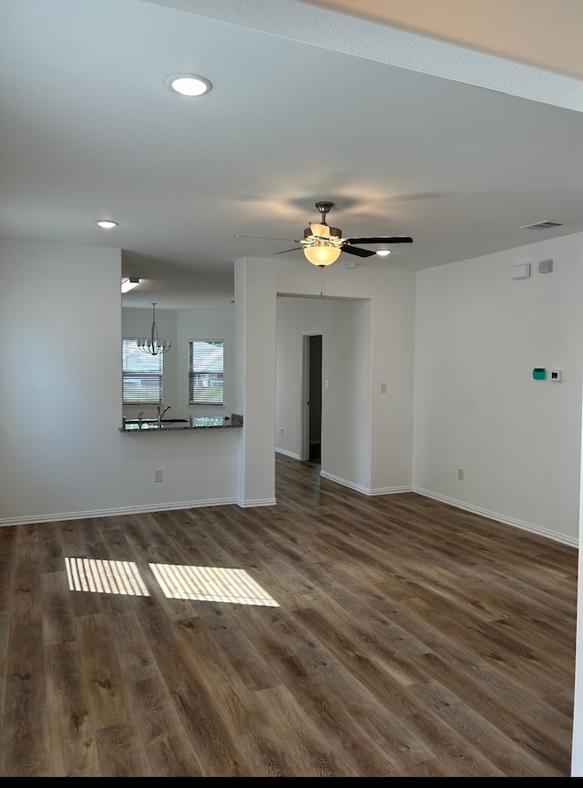 unfurnished living room featuring ceiling fan with notable chandelier and dark hardwood / wood-style floors