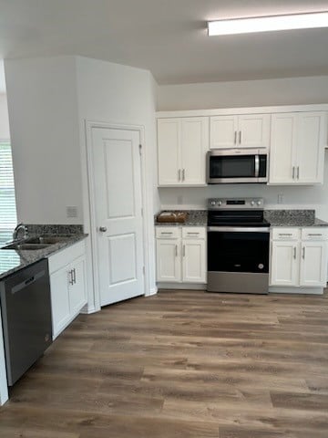 kitchen with white cabinets, sink, stainless steel appliances, dark hardwood / wood-style floors, and dark stone countertops