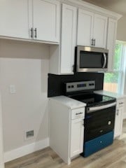 kitchen featuring black range with electric stovetop, light hardwood / wood-style floors, and white cabinetry