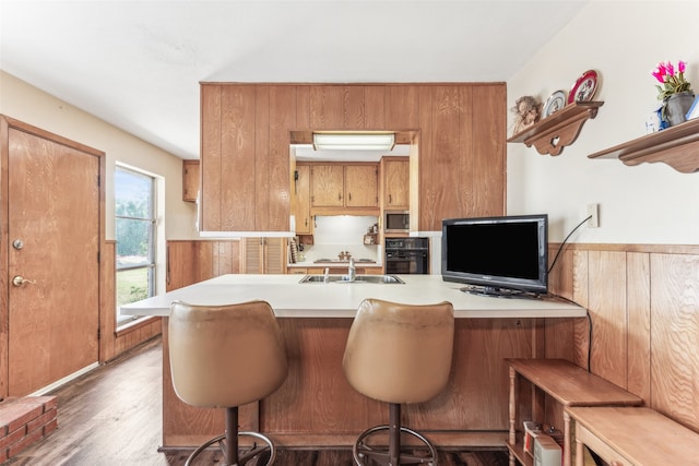 kitchen with a kitchen bar, kitchen peninsula, dark wood-type flooring, black oven, and sink