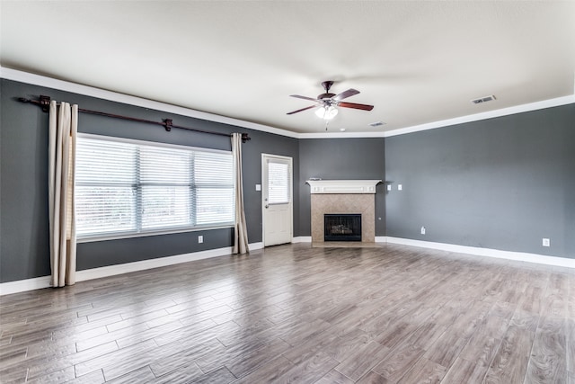 unfurnished living room with ornamental molding, a tile fireplace, hardwood / wood-style flooring, and a healthy amount of sunlight