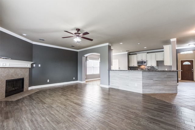 unfurnished living room with crown molding, wood-type flooring, a tile fireplace, and ceiling fan