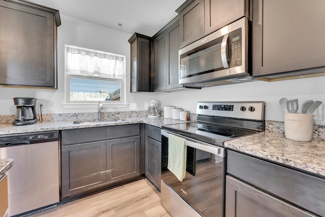 kitchen featuring light hardwood / wood-style floors, appliances with stainless steel finishes, sink, and light stone countertops