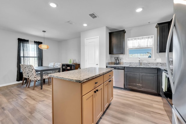 kitchen with appliances with stainless steel finishes, light brown cabinetry, light hardwood / wood-style floors, a kitchen island, and sink