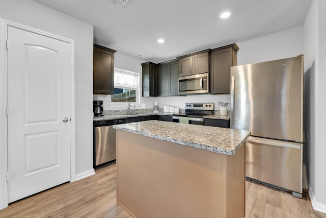 kitchen featuring dark brown cabinetry, stainless steel appliances, light stone countertops, light hardwood / wood-style floors, and a kitchen island