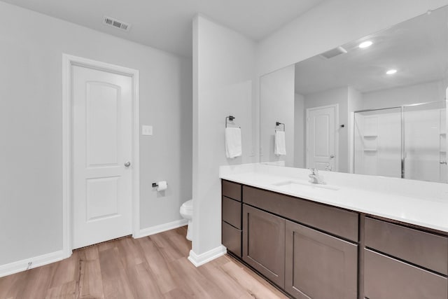 bathroom featuring vanity, wood-type flooring, a shower with shower door, and toilet