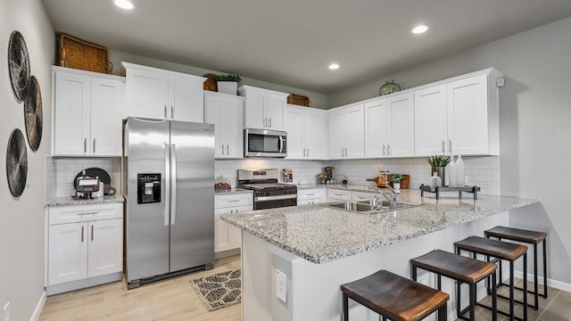 kitchen with appliances with stainless steel finishes, white cabinets, a breakfast bar area, and decorative backsplash