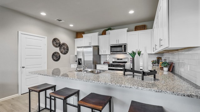 kitchen featuring tasteful backsplash, appliances with stainless steel finishes, white cabinets, light hardwood / wood-style flooring, and sink