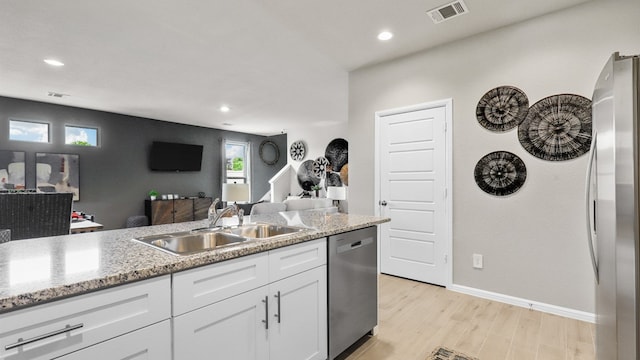 kitchen with appliances with stainless steel finishes, light hardwood / wood-style floors, light stone counters, sink, and white cabinets