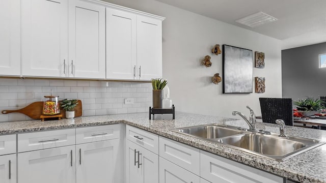 kitchen featuring light stone counters, decorative backsplash, sink, and white cabinetry