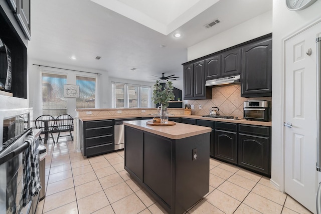 kitchen featuring light tile patterned flooring, under cabinet range hood, a peninsula, visible vents, and backsplash