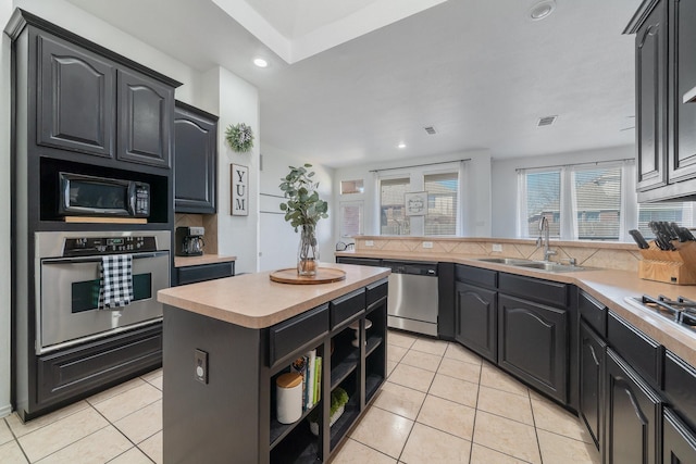 kitchen featuring light tile patterned floors, backsplash, stainless steel appliances, light countertops, and a sink