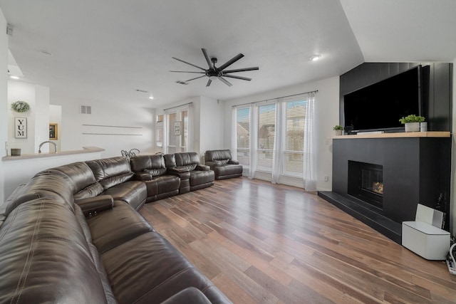 living area featuring lofted ceiling, recessed lighting, visible vents, a glass covered fireplace, and wood finished floors