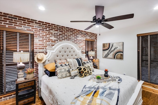 bedroom featuring ceiling fan, wood-type flooring, and brick wall