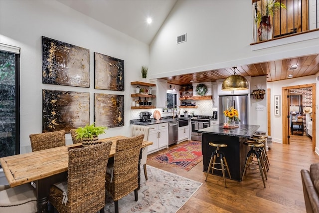 dining space with wooden ceiling, high vaulted ceiling, sink, and light wood-type flooring