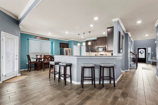 kitchen with pendant lighting, appliances with stainless steel finishes, hardwood / wood-style floors, light stone countertops, and dark brown cabinetry