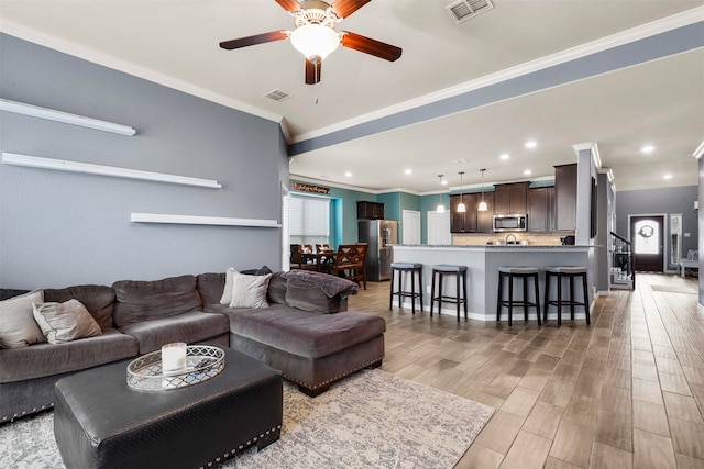 living room with ceiling fan, ornamental molding, and light hardwood / wood-style floors