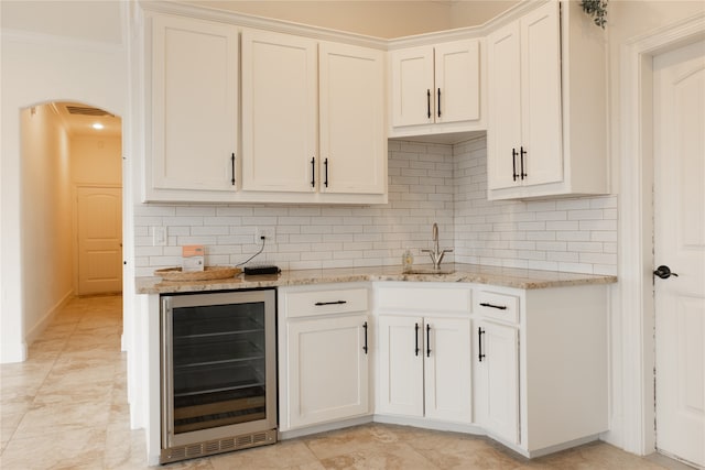 kitchen with tasteful backsplash, light stone countertops, wine cooler, light tile patterned floors, and crown molding