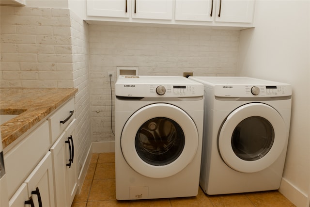 clothes washing area featuring independent washer and dryer, brick wall, light tile patterned floors, and cabinets